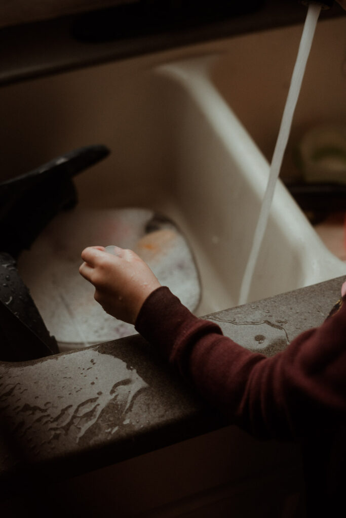 cinematic image of a boy playing with water at a sink while it rains outside